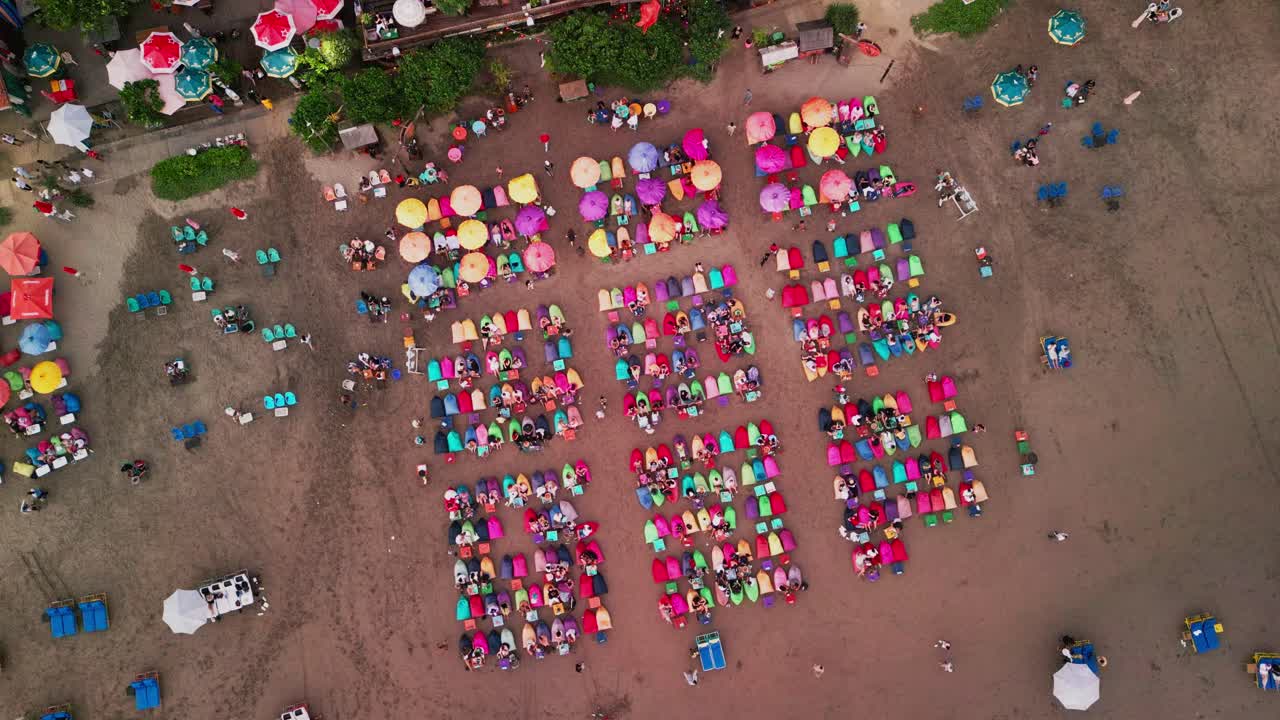 The golden hour casts long shadows over Seminyak’s famous shoreline where beach umbrellas create a vibrant pattern across the sand as seen from a peaceful drone view above the sea