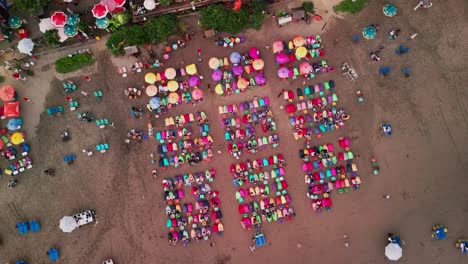 the golden hour casts long shadows over seminyak’s famous shoreline where beach umbrellas create a vibrant pattern across the sand as seen from a peaceful drone view above the sea
