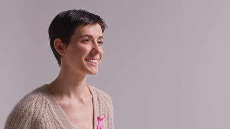 Studio-Portrait-Of-Smiling-Young-Woman-Wearing-Pink-Breast-Cancer-Awareness-Ribbon-Against-White-Background-2