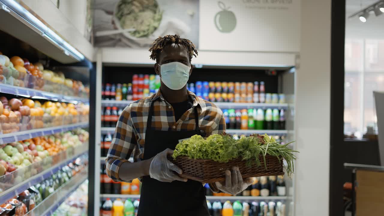 Employé masqué dans le magasin marchant avec un panier rempli de légumes verts.