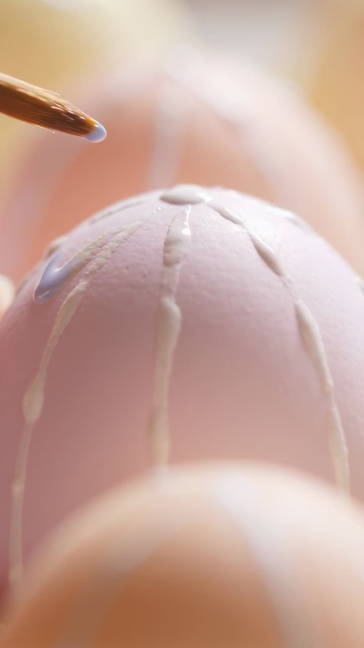 Vertical video: Approaching brush leading hand applying pale dots and lines on pink egg decorating