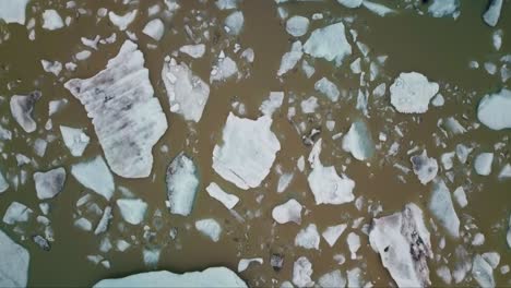 Top-down-flyover-of-massive-blue-iceberg-floating-in-a-muddy-glacier-lagoon-in-Iceland