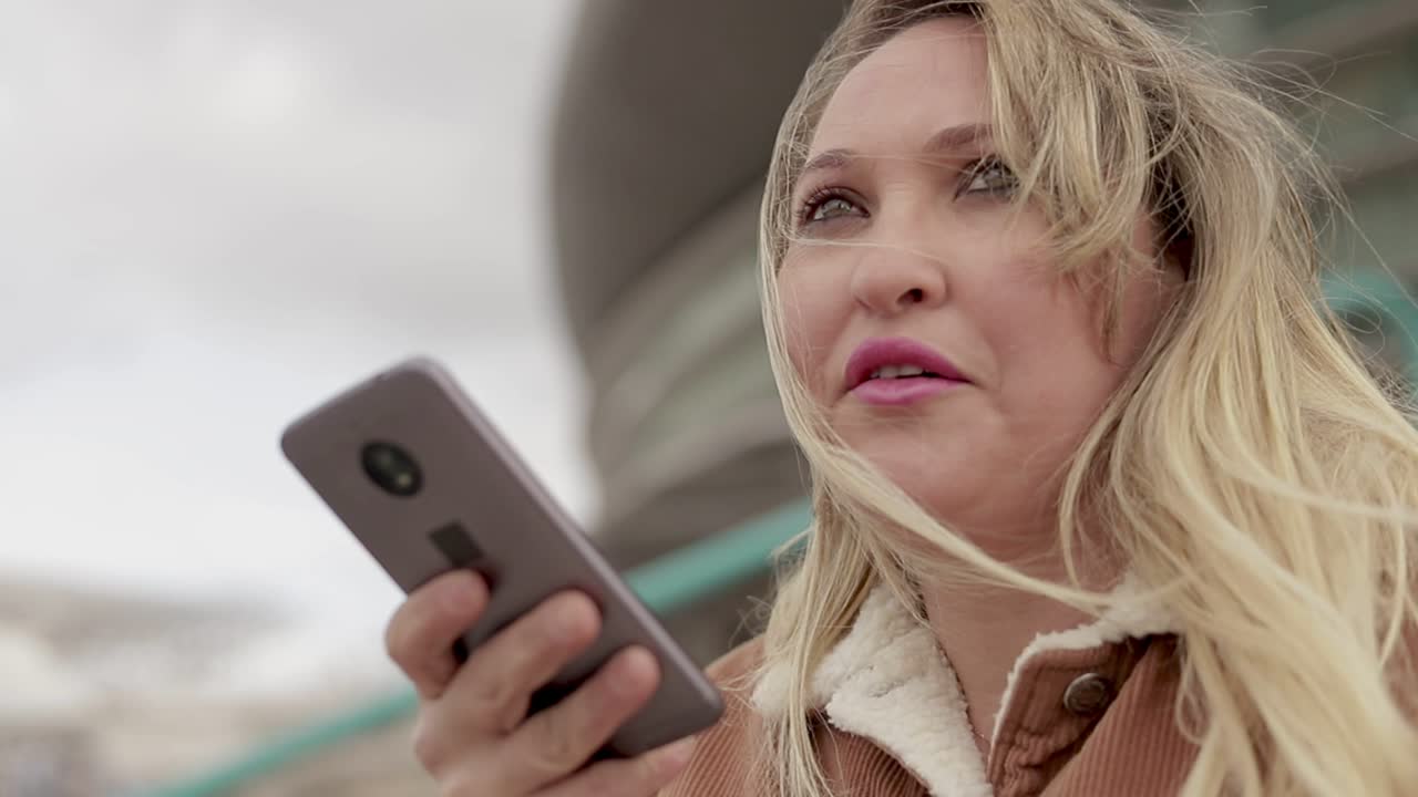 Smilende midaldrende kvinde taler i smartphone udendørs