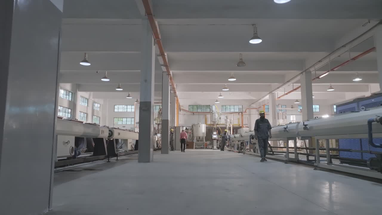Low angle view of workers in a modern PVC pipe manufacturing factory. The image showcases industrial machinery and spacious factory interiors in Karachi, Pakistan.