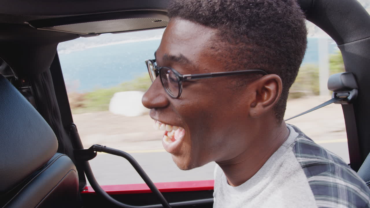 젊은 남성 승객이 여름 휴가 중 오픈  렌터카의 뒷좌석에서 재미를 느끼고 있습니다.