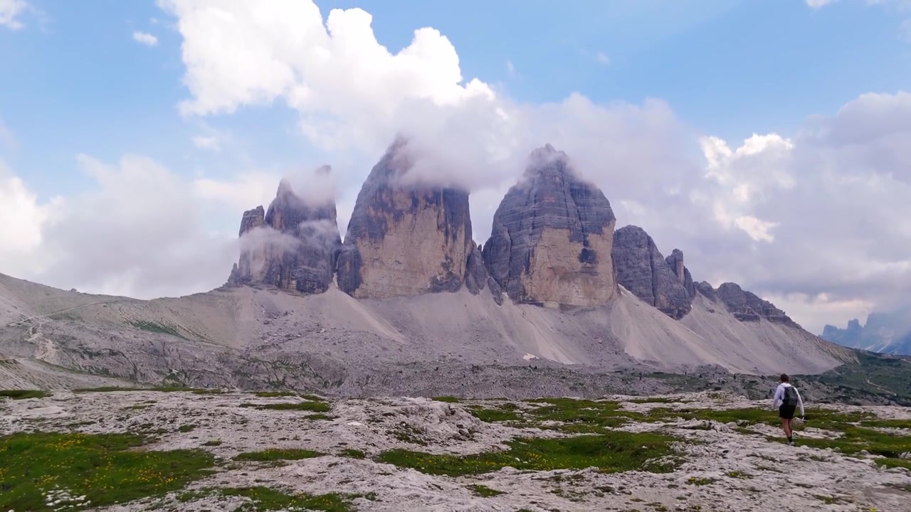 Ripresa con drone che si avvicina e si inclina verso l'alto per rivelare un viaggiatore solitario che cammina verso le Dolomiti