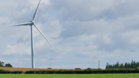 a large wind turbine spins steadily in a rural landscape near edinburgh, scotland. daylight, wide shot, static camera, cloudy sky, green fields