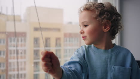 cute european child is looking out window in snowy winter day watching how snow falling