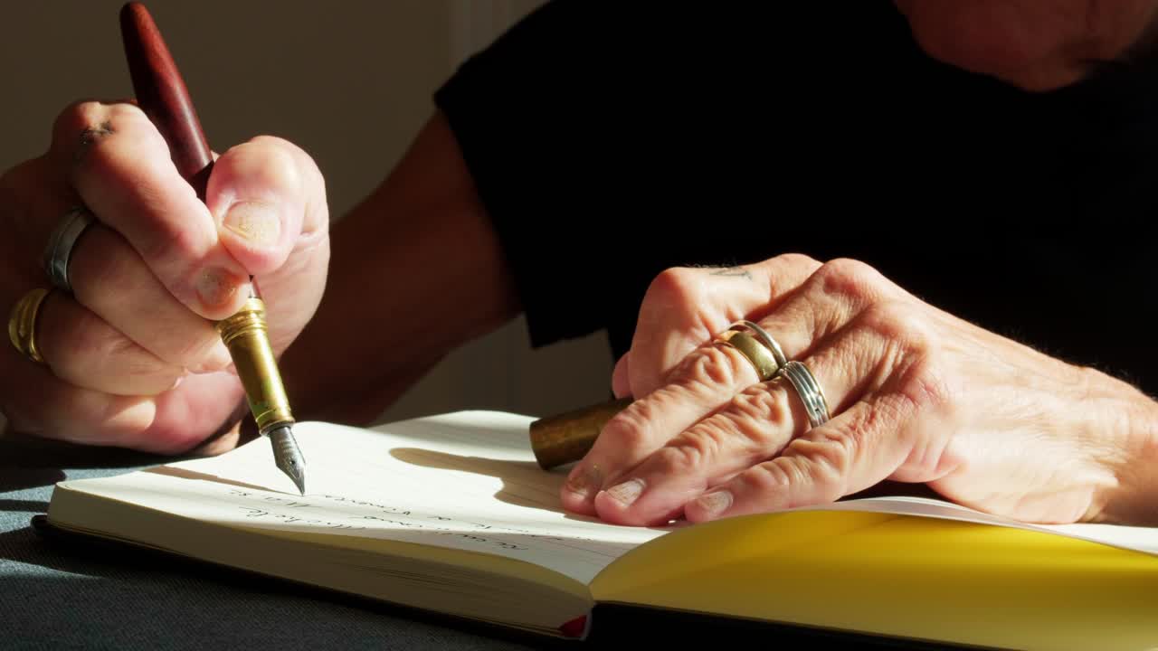 Primo piano di mani anziane che scrivono in un quaderno usando una penna stilografica. Elegante scatto di una persona anziana che scrive un diario o firma un documento con una classica penna a inchiostro e cancelleria vintage.
