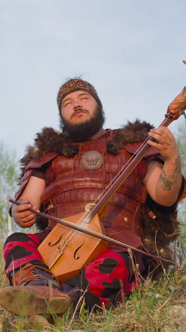 Meditating performer in ethnic clothes plays local lyre instrument sitting on green grass. Spiritual music to clear mind. Harmony with nature