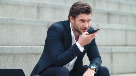 businessman recording voice message on cellphone in city. man sitting on stairs