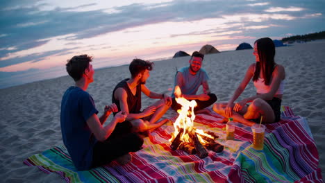 friends enjoying a beach bonfire with music at sunset