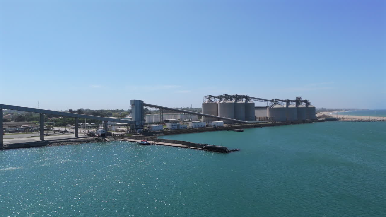 drone móvil derecho disparado junto a grandes silos de almacenamiento en el puerto de necochea, argentina. océano tranquilo y cielos azules soleados. disparado 4k-60fps.