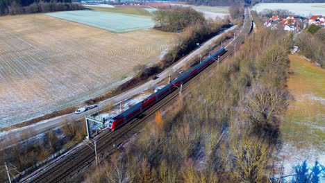 red passenger train traversing through rural frosted countryside