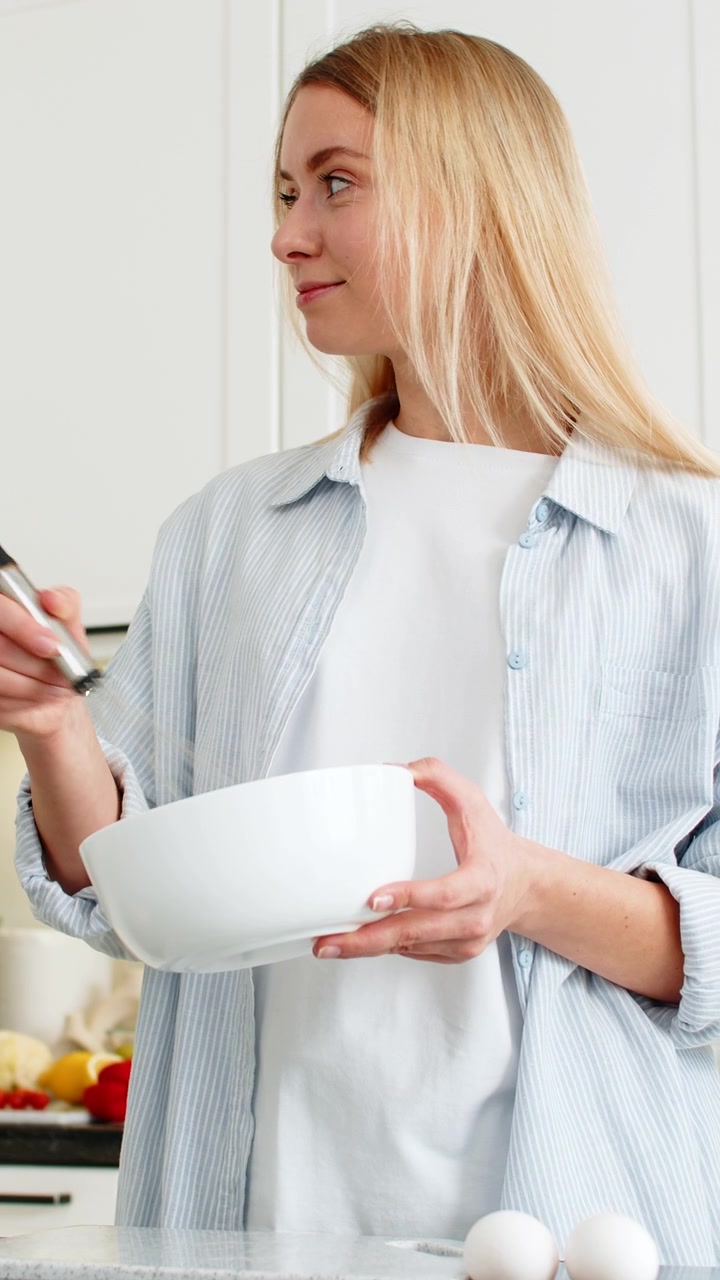 Young woman whisking eggs in bowl in modern home kitchen preparing omelet batter for quick breakfast