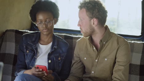 An-Young-Woman-Talks-With-A-Guy-In-A-Caravan-While-Watching-Her-Cellphone-1