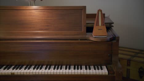 antique vintage wooden metronome swings its pendulum at 60bpm on top of old rustic brown piano