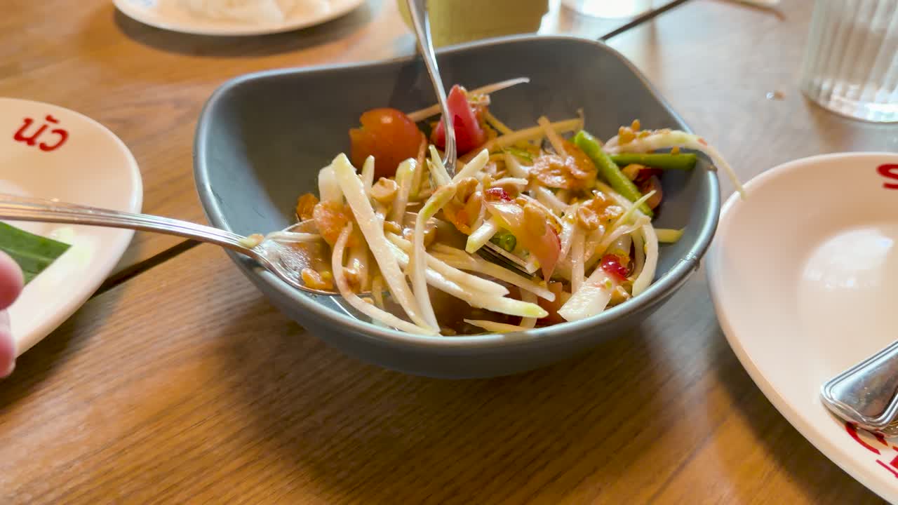 Hand scoops som tum salad from bowl in bright, casual Bangkok restaurant with natural lighting