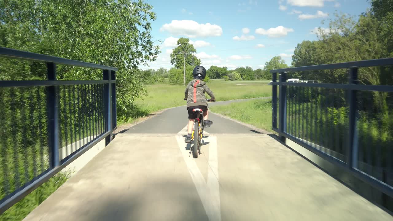 Following young boy on bicycle over bridge and paved trail, POV