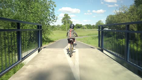 following young boy on bicycle over bridge and paved trail, pov
