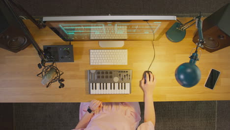 overhead view of female musician at computer with keyboard and microphone in studio at night