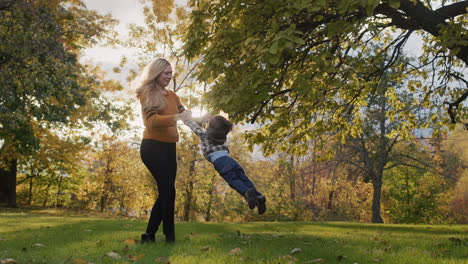 active young mother having fun with her little son in the park - holding his hands and circling