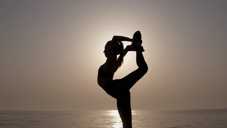 silueta de una mujer sobresaliente. vista frontal de una chica estirándose y practicando, haciendo un hilo vertical, dobla su pierna. amanecer