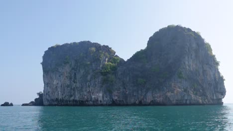 ultra slow motion shot tilting up from water to giant limestone rock with vegetation in thailand