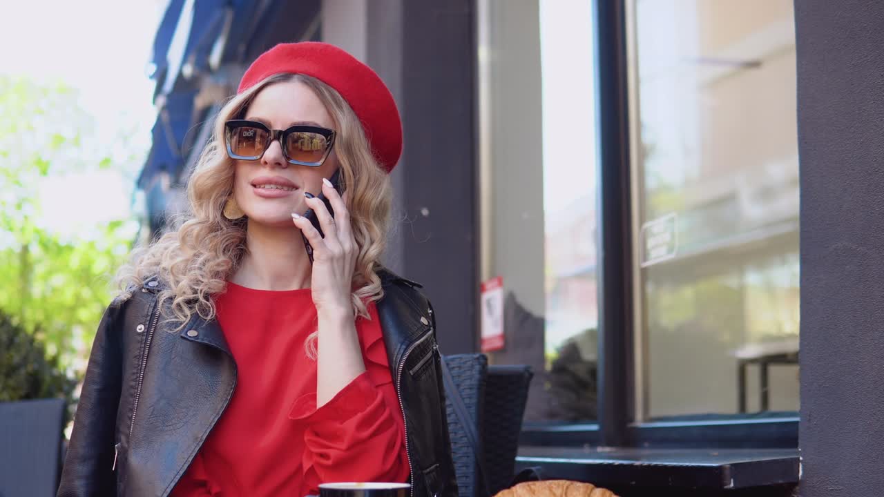 Coffee break with croissant. Modern urban young woman talking on cell phone on a cozy street