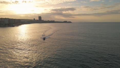 A-boat-sails-along-the-coastline-of-Sliema,-Malta-as-the-setting-sun-reflects-off-the-water