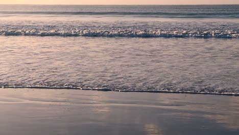 Videoaufnahme-Von-Meereswellen,-Die-Am-Strand-Entlang-Krachen,-Mit-Strahlen-Aus-Flachem-Sonnenlicht