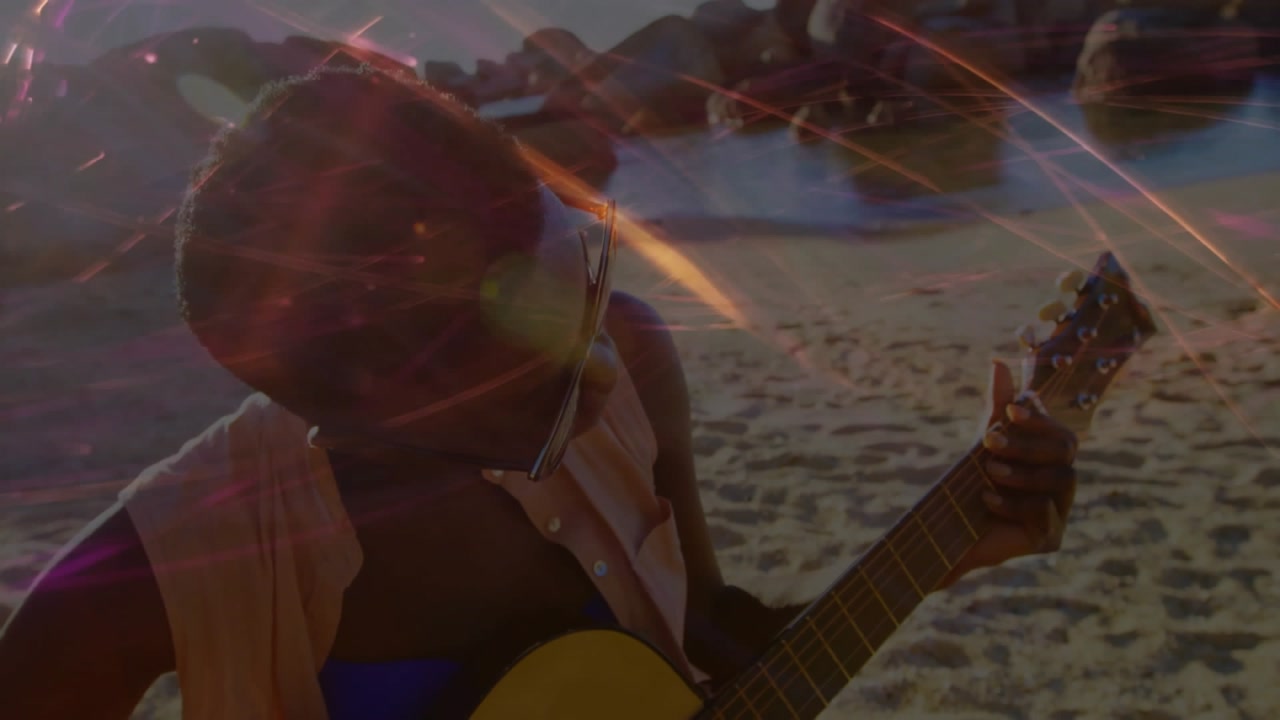 Woman strumming guitar on sandy beach at sunset, showing pink orange light overlays for marketing