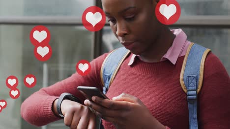 Animation-of-social-media-heart-icons-over-african-american-woman-using-smartphone-in-city-street