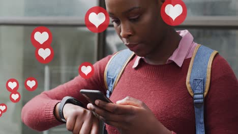 animation of social media heart icons over african american woman using smartphone in city street