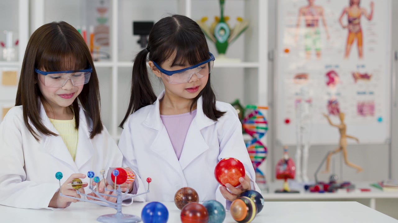 Asian students wear safety goggles and lab coats while examining a planetary model in classroom.