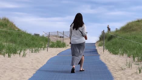 a woman is walking away from the camera at a beach with a blue mat placed on the sand.