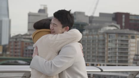 young asian couple meeting and hugging on millennium bridge in london uk