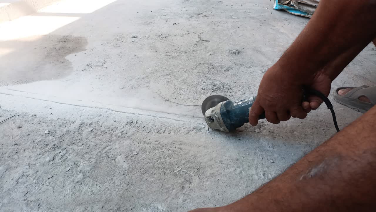 Close up of worker hand using grinder cutting concrete floor with electric saw to lay electrical wiring