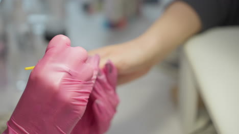 closeup of nail technician wearing pink gloves working on customer nails with precision tool while engaging in conversation, highlighting focus, communication, and customer service in salon setting