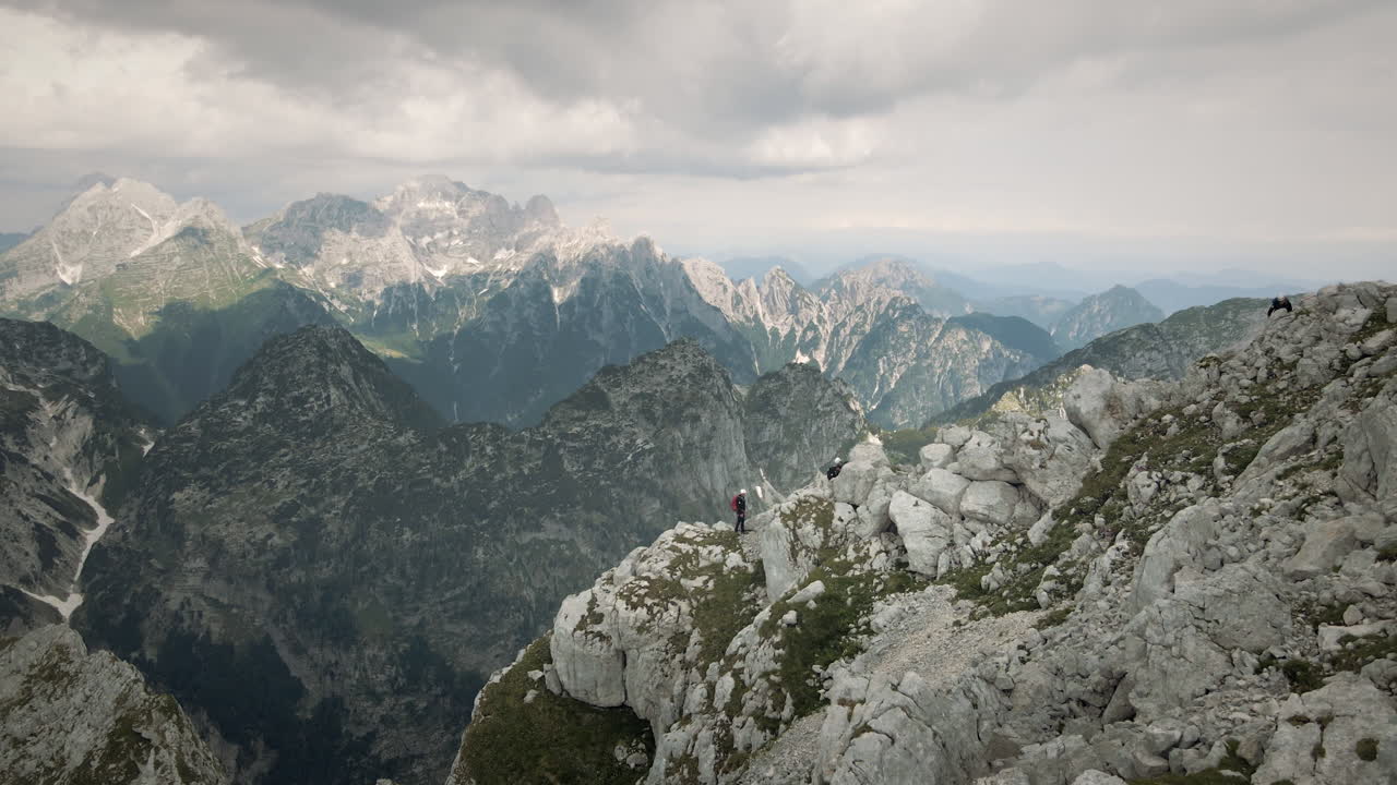 tiro de drones de montañas, grupo de excursionistas escalando una montaña, algún rayo de sol en el fundamento de otras montañas, las nubes están cubriendo el cielo