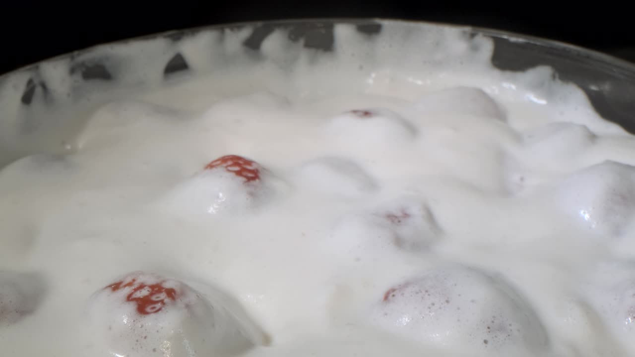 검은색 배경의 유리 용품에 두꺼운 크림 층으로 인 익은 딸기를 회전합니다. 카메라 회전 360도, 클로즈업.