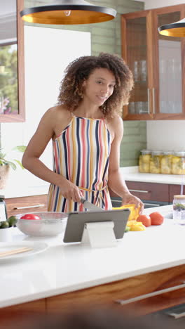 vertical video: a young woman with curly hair is using a tablet in the kitchen