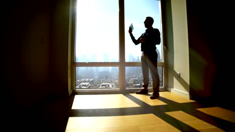 outlines of man opening blinds on big windows. sun shines into the room, producing shadows.