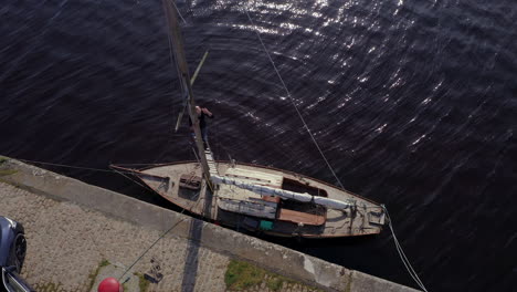 drone top shot overview of man working at mast of damaged sailboat, dark sea surface and rope details