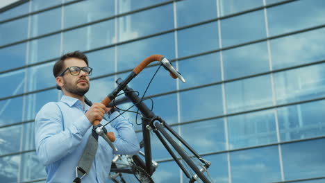 attractive young man, office worker, walking and carrying his bicycle near a modern office center