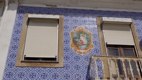 facade with blue azulejo tiles and guardian angel image with shuttered windows and weathered balcony railing. aveiro, portugal. low angle shot