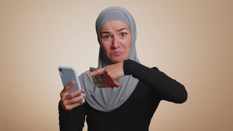 happy muslim woman use smartphone rejoicing win, receiving money dollar cash, success lottery luck