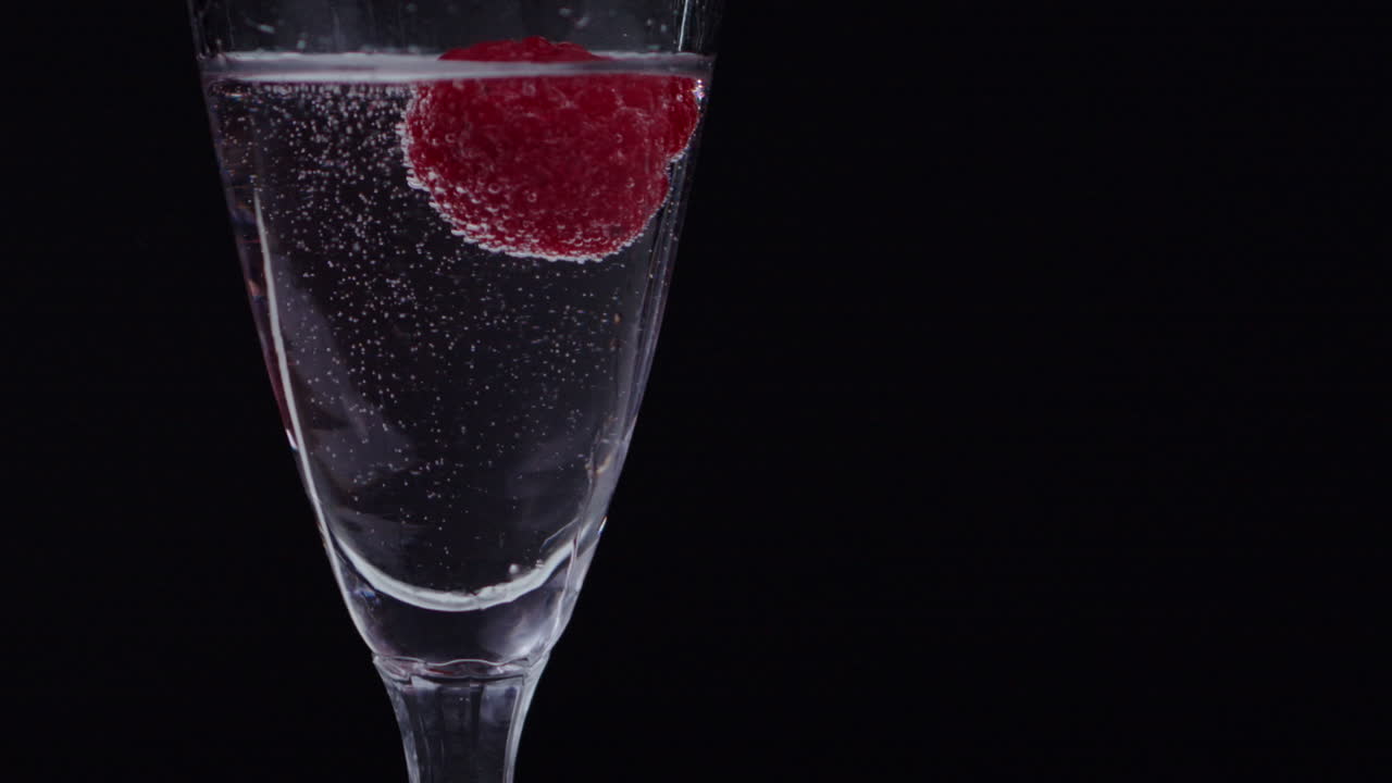 Lampone congelato che galleggia lentamente in un bicchiere d'acqua pieno di bolle d'ossigeno