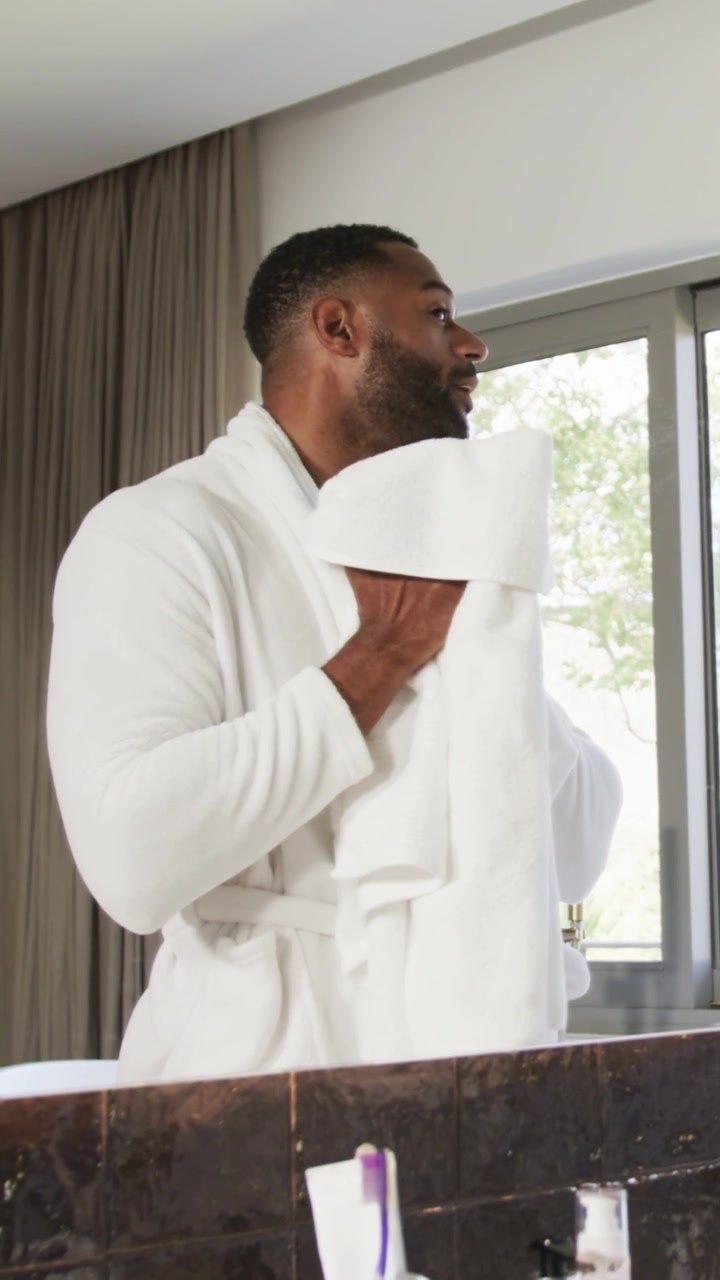 Vertical video: Lifting white towel, man in white bathrobe drying and wiping face at bathroom sink