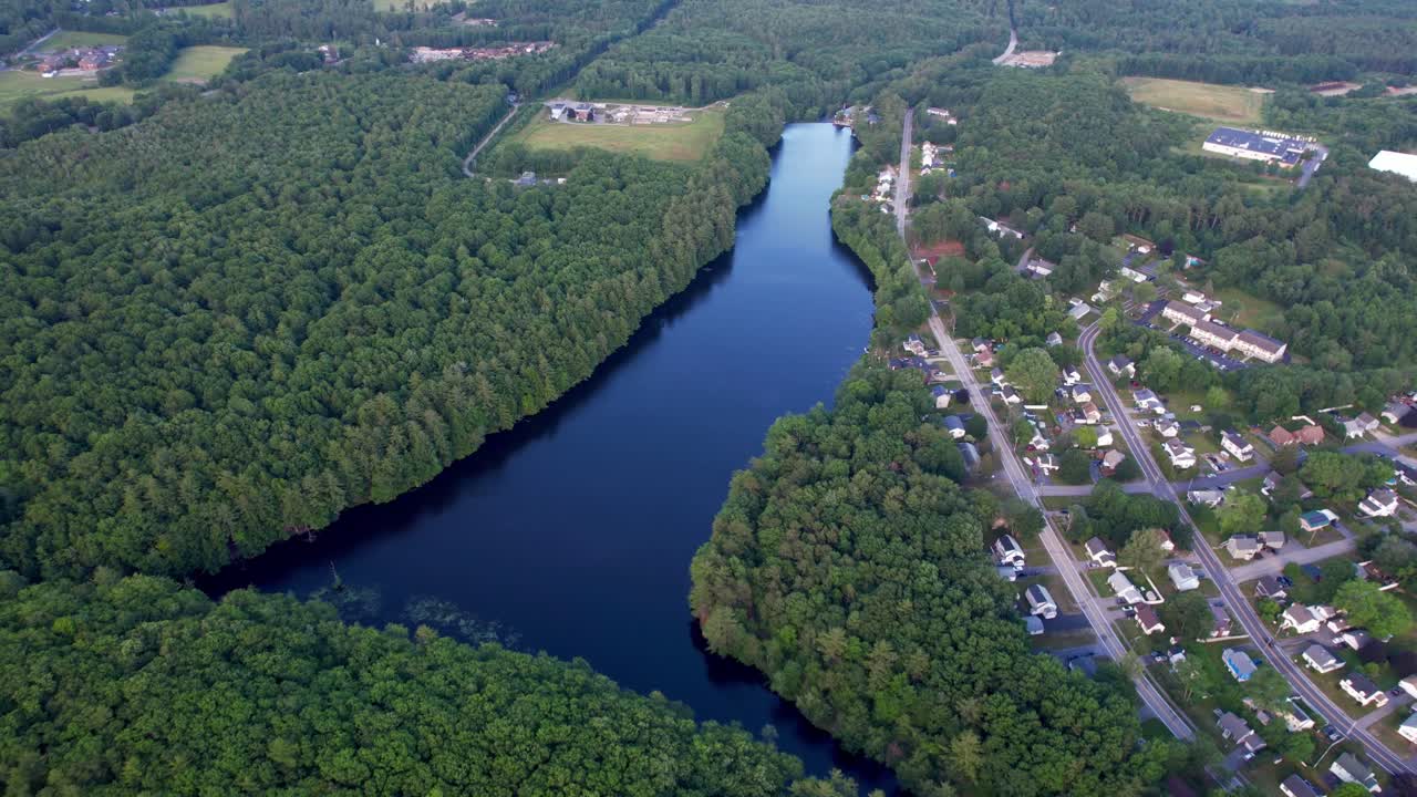 Aerial view shows forest lake with winding shoreline, marsh clearing, lush green trees, waterside neighborhood, dense foliage, tranquil nature, scenic summer landscape